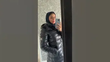 Moncler Moka long black shiny puffy hooded down jacket. Girl in a winter shiny down jacket.